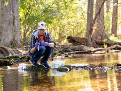 Ronny Saunders crouches while standing on a rock in a creek