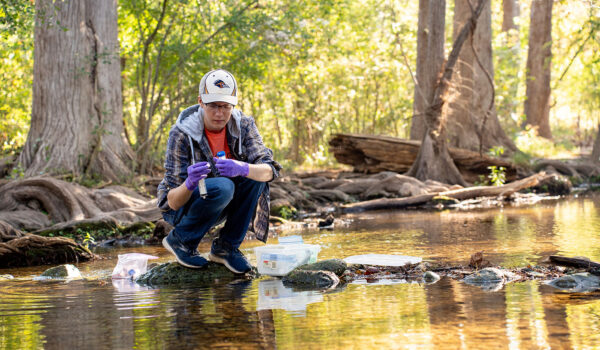 Ronny Saunders crouches while standing on a rock in a creek