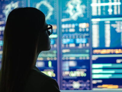 A woman in glasses looks at a series of brightly-colored monitors