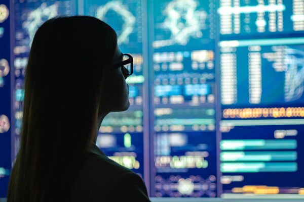 A woman in glasses looks at a series of brightly-colored monitors