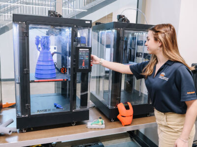 A woman reaches up towards a 3-D printer.