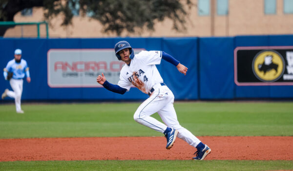 A young man in a baseball uniform runs to the left on a baseball field.