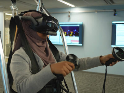 Doctoral student Nipa Anjum stands on a balancing board while wearing a VR headset.