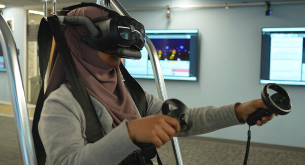 Doctoral student Nipa Anjum stands on a balancing board while wearing a VR headset.