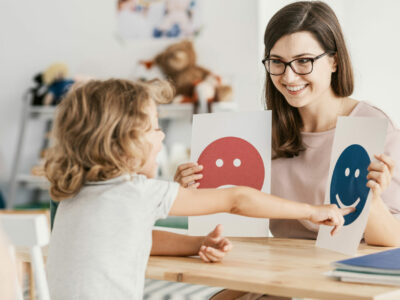 A behavioral analyst holds up a smiling face and a frowning face in front of a child who points to the smiling face.