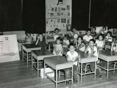 Black and white photo of elementary students sitting in a classroom at their individual desks.