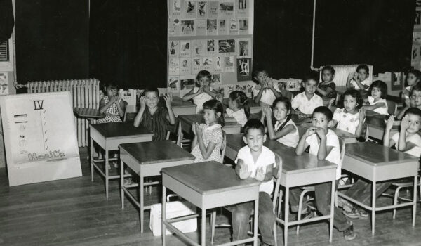 Black and white photo of elementary students sitting in a classroom at their individual desks.
