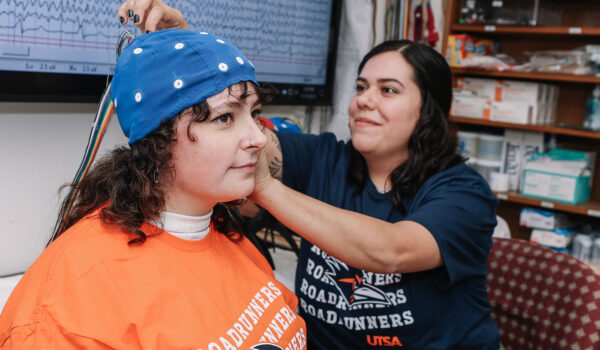 A UTSA researcher adjusts an EEG cap atop a subject's head