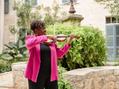Nicole Cherry smiles while playing her violin in a courtyard at the UTSA Southwest Campus.