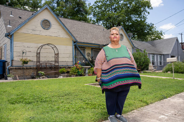 A lady stands on her front lawn and looks off to the side.